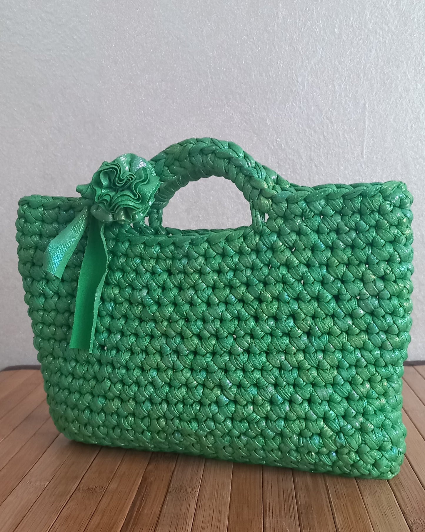 Una piccola borsa lavorata all'uncinetto con una trama fissa e un fiore vicino alla maniglia è in piedi su un tavolo di lagno