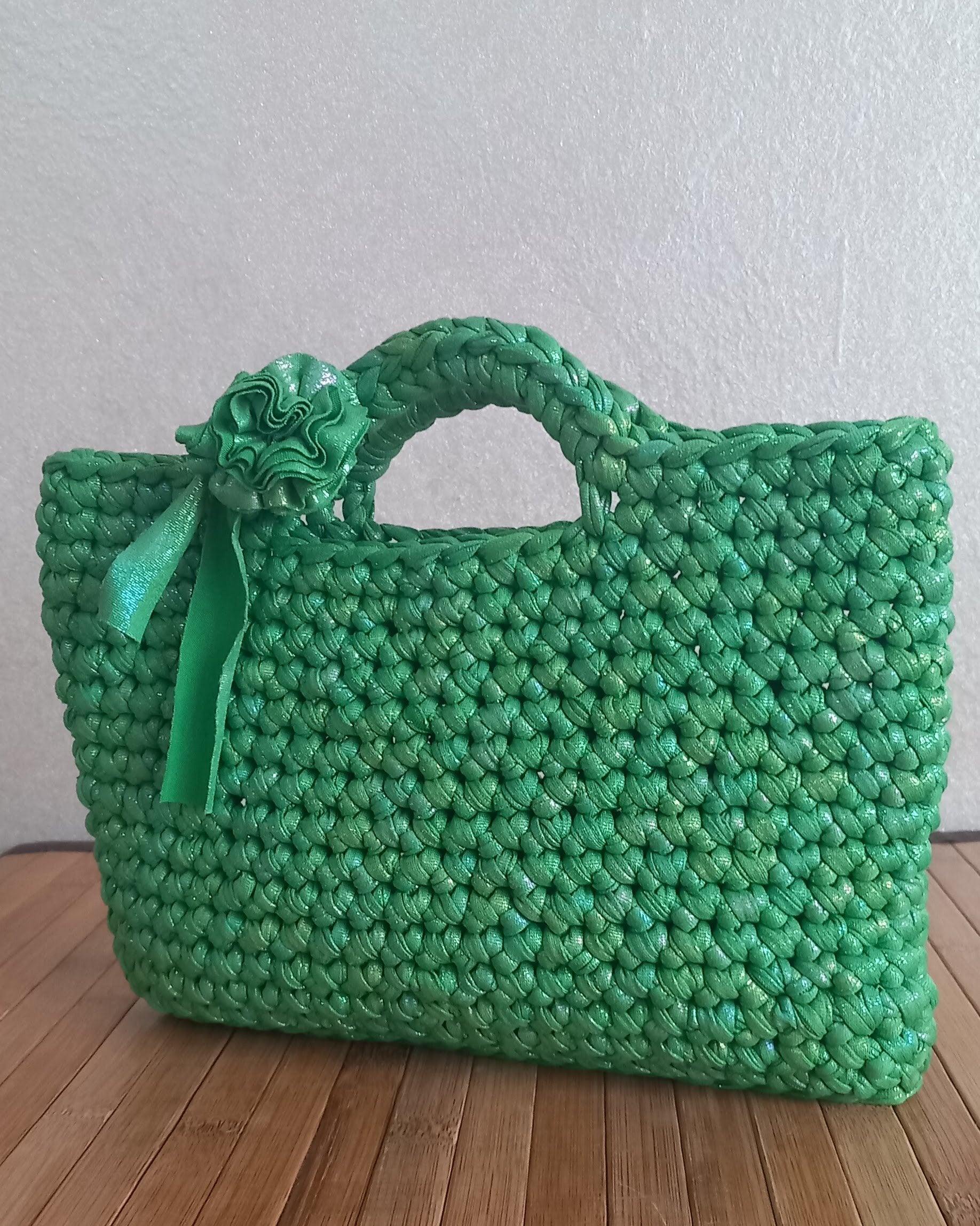 Una piccola borsa lavorata all'uncinetto con una trama fissa e un fiore vicino alla maniglia è in piedi su un tavolo di lagno