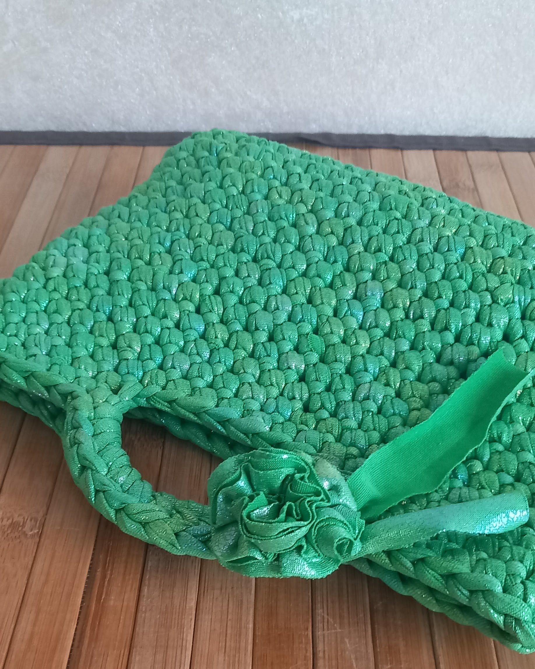 una mini bag lavorata all'uncinetto con un fiore vicino al manico appoggiata su un suporto di legno.